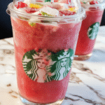 A vibrant pink Starbucks Pink Flamingo Refresher in a clear glass with ice cubes, garnished with a slice of lime and fresh berries, set on a sunny outdoor table with a blurred summer background.